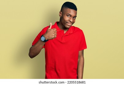 Young African American Man Wearing Casual Red T Shirt Doing Happy Thumbs Up Gesture With Hand. Approving Expression Looking At The Camera Showing Success. 