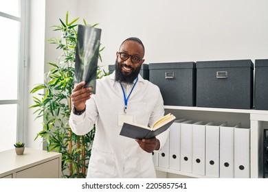 Young African American Man Wearing Doctor Uniform Holding Book Looking Xray At Clinic