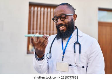 Young African American Man Wearing Doctor Uniform Using Smartphone At Hospital