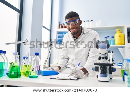 Young african american man wearing scientist uniform weighing diamond at laboratory