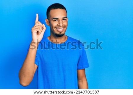 Young african american man wearing casual blue t shirt pointing finger up with successful idea. exited and happy. number one. 