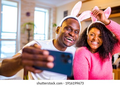 Young african american man and woman wearing cute easter bunny ears in the house taking selfie on smartphone