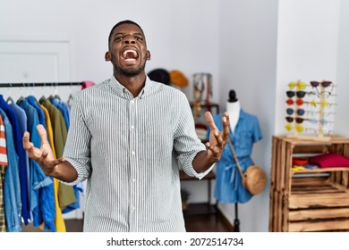 Young african american man working as manager at retail boutique crazy and mad shouting and yelling with aggressive expression and arms raised. frustration concept. 