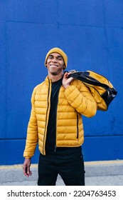 Young African American Man With Yellow Winter Sport Coat Holding A Yellow Travel Bag Posing Over Blue Background