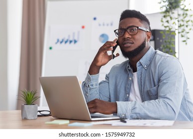 Young African American Manager Working On Laptop And Talking On Phone With Concerned Face Expression, Having Hard Day At Work