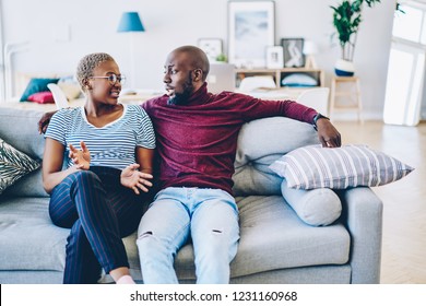 Young african american marriage having discussion about problem sitting at couch in living room, romantic couple talking about relationship looking at each other spending time together at living room 