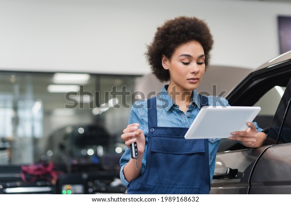 young african american mechanic holding digital\
tablet and car key in\
garage