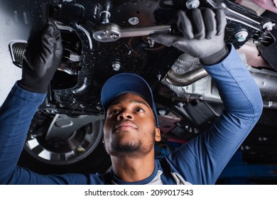 Young african american mechanic working with tool under car in garage