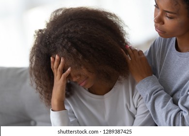 Young African American mom hug disappointed sad teenage daughter, caressing and comforting her, black teen girl feel down, suffer from school problems, mommy or nanny embrace and support