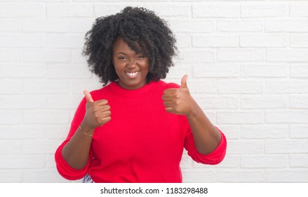 Young african american plus size woman over white brick wall success sign doing positive gesture with hand, thumbs up smiling and happy. Looking at the camera with cheerful expression, winner gesture. - Powered by Shutterstock