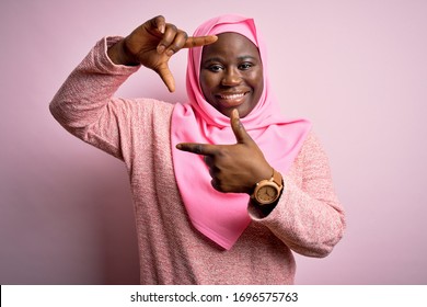 Young African American Plus Size Woman Wearing Muslim Hijab Over Isolated Pink Background Smiling Making Frame With Hands And Fingers With Happy Face. Creativity And Photography Concept.