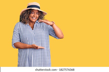 Young african american plus size woman wearing summer hat gesturing with hands showing big and large size sign, measure symbol. smiling looking at the camera. measuring concept. 