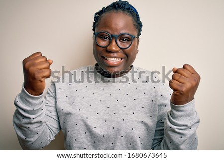 Young african american plus size woman with braids wearing casual sweatshirt and glasses celebrating surprised and amazed for success with arms raised and open eyes. Winner concept.