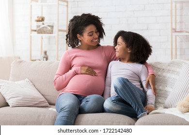 Young african american pregnant woman bonding with her little daughter at home, sitting on couch and hugging, free space - Powered by Shutterstock