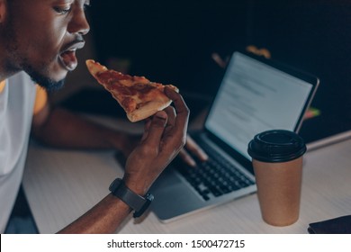 Young African American Programmer Eating Pizza While Sitting At Workplace