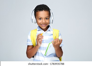 Young African American school boy writing in notepad with headphones and backpack on grey background - Powered by Shutterstock