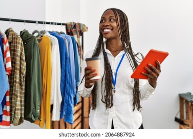 Young african american shopkeeper woman using touchpad and drinking coffee at clothing store.