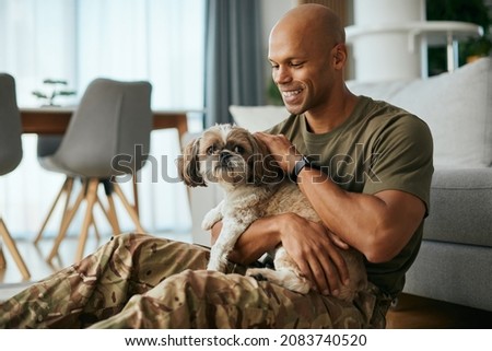 Young African American soldier cuddling his dog while spending time together at home.