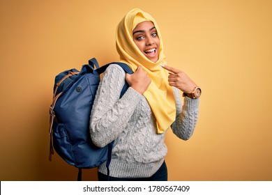 Young African American Student Girl Wearing Muslim Hijab And Backpack Over Yellow Background Very Happy Pointing With Hand And Finger