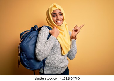 Young African American Student Girl Wearing Muslim Hijab And Backpack Over Yellow Background Very Happy Pointing With Hand And Finger To The Side