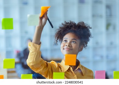 Young African American stylish woman working on project plan using sticky papers notes on glass wall, people meeting to share idea, Business design planning concepts. - Powered by Shutterstock