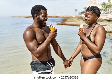 Young african american tourist couple wearing swimwear eating ice cream at the beach.