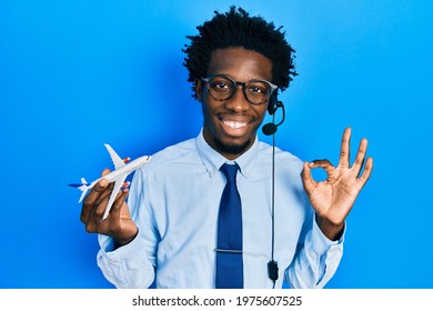 Young african american travel agent man holding plane doing ok sign with fingers, smiling friendly gesturing excellent symbol 