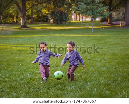 Young African American twin boys playing soccer in public park in fall