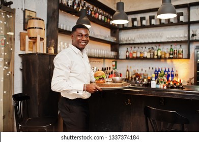 Young African American Waiter Man Hold Tray With Burger At Bar Of Restaurant.