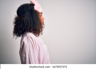 Young African American Woman With Afro Hair Wearing Sleeping Eye Mask And Pink Pajama Looking To Side, Relax Profile Pose With Natural Face With Confident Smile.