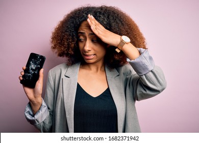 Young african american woman with afro hair holding cracked and broken smartphone screen stressed with hand on head, shocked with shame and surprise face, angry and frustrated. Fear and upset