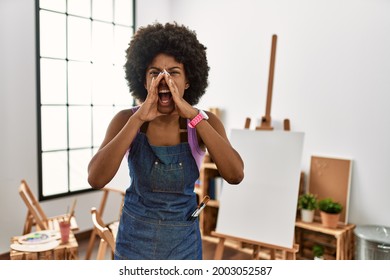 Young african american woman and afro hair at art studio shouting angry out loud and hands over mouth 