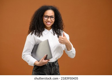 Young African American Woman With Afro Hairstyle Wearing Smart Casual Wear Standing Isolated On Brown And Showing Big Finger, Carrying Laptop Computer, Smiling, Female Office Employee, Student