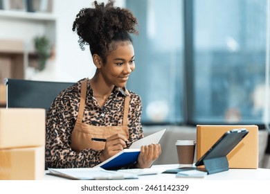 A young African American woman with afro brown hair works in a modern office, managing her small business, utilizing laptop technology for e-commerce, shipping, and marketing, sme box.