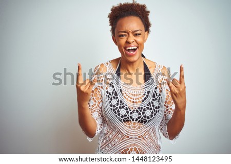 Young african american woman with afro hair wearing a bikini over white isolated background shouting with crazy expression doing rock symbol with hands up. Music star. Heavy concept.