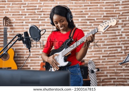 Young african american woman artist singing song playing electrical guitar at music studio