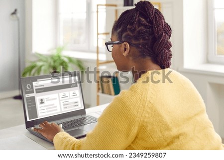 Young African American woman with beautiful Afro braids sitting at desk at home, using laptop computer, browsing online banking website, visiting business account page, and updating personal details [[stock_photo]] © 