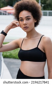 Young African American Woman In Black Sports Bra And Fitness Tracker Standing With Hand Near Face