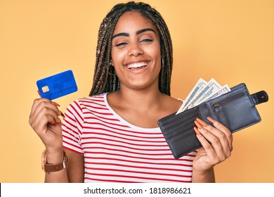 Young african american woman with braids holding wallet with dollars and credit card smiling and laughing hard out loud because funny crazy joke. 