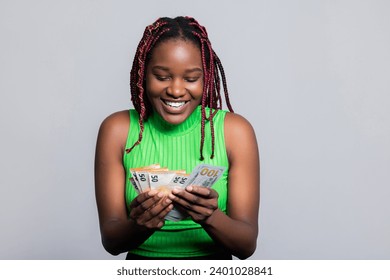 Young African American woman with colourful stylish braids counting money holding bunch of dollars in hands smiling celebrating the first salary. - Powered by Shutterstock