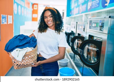 Young african american woman with curly hair smiling happy doing chores at the laundry