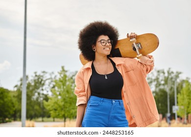 A young African American woman with curly hair holds a skateboard up to her face in a skate park. - Powered by Shutterstock