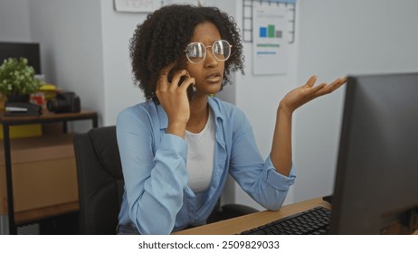 Young african american woman with curly hair talking on the phone in an office setting, wearing eyeglasses and a blue shirt, raising her hand in a questioning gesture. - Powered by Shutterstock