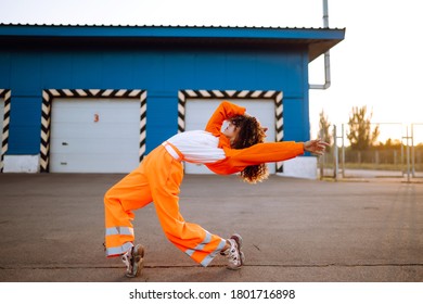 Young African American woman - dancer dancing in the street at sunset. Stylish woman with curly hair in an orange suit  showing some moves. Sport, dancing and urban culture concept. - Powered by Shutterstock