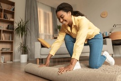 Young African American Woman Doing The Housekeeping, Bending Down And Rolling Carpet In A Living Room, Preparing To Cleaning The Floor, Copy Space