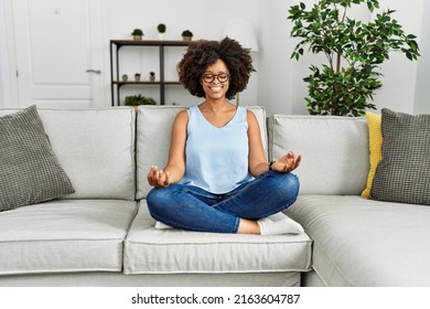 Young African American Woman Doing Yoga Sitting On Sofa At Home