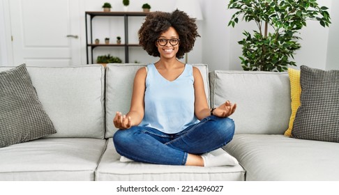 Young African American Woman Doing Yoga Sitting On Sofa At Home