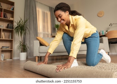 Young african american woman doing the housekeeping, bending down and rolling carpet in a living room, preparing to cleaning the floor, copy space - Shutterstock ID 2251155753