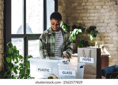 Young African American woman is doing garbage waste sorting at home. Concept of sustainable lifestyle, daily routine to protect planet from pollution, domestic life, simple actions for environment - Powered by Shutterstock