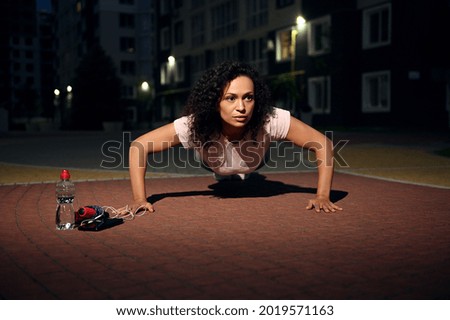 Young african american woman doing push-ups during evening workout on the sports ground. Active and healthy lifestyle concept. Outdoor workout